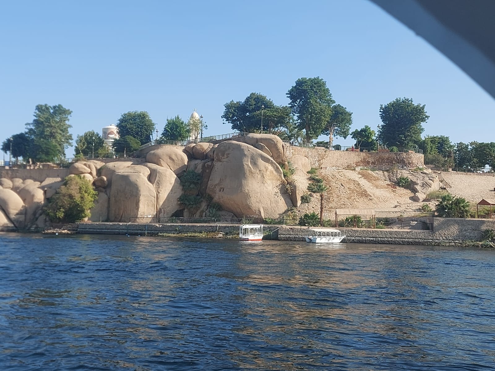 Blick über den Nil auf Felsen, Bäume und zwei Boote am Ufer