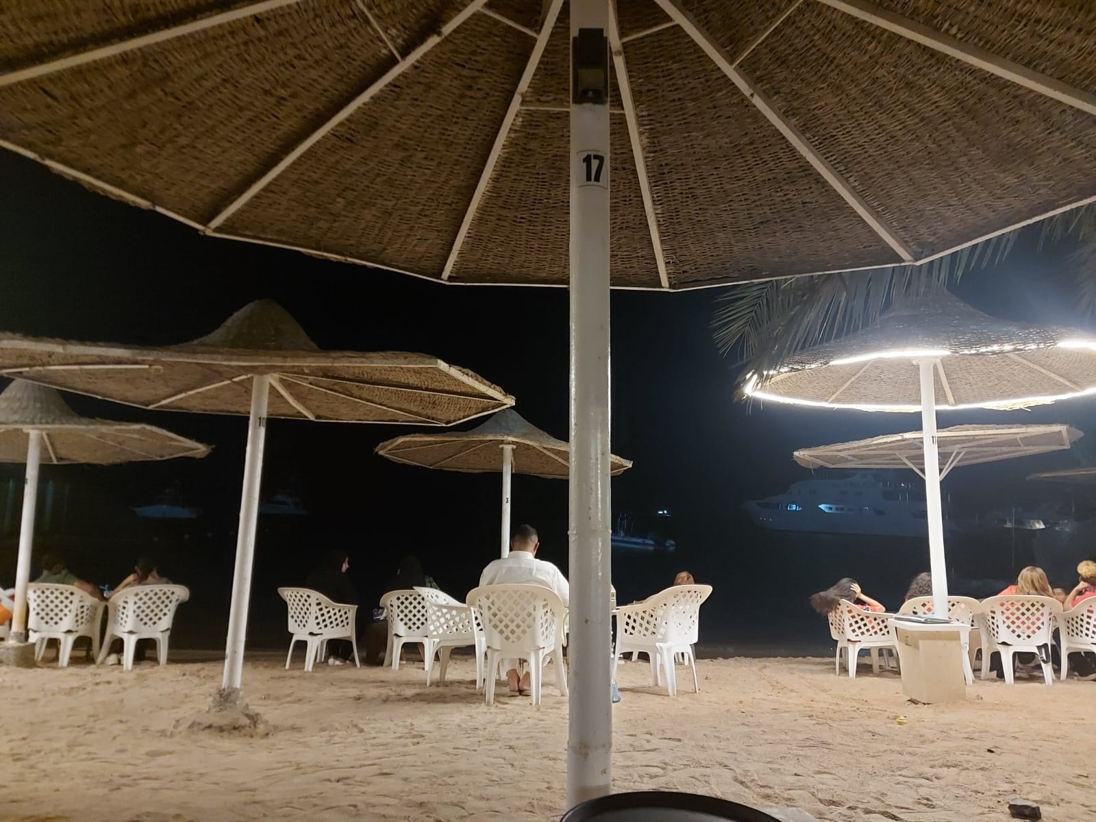 Ein Strandlokal am Abend: Stühle unter Schilfschirmen, dahinter das dunkle Meer